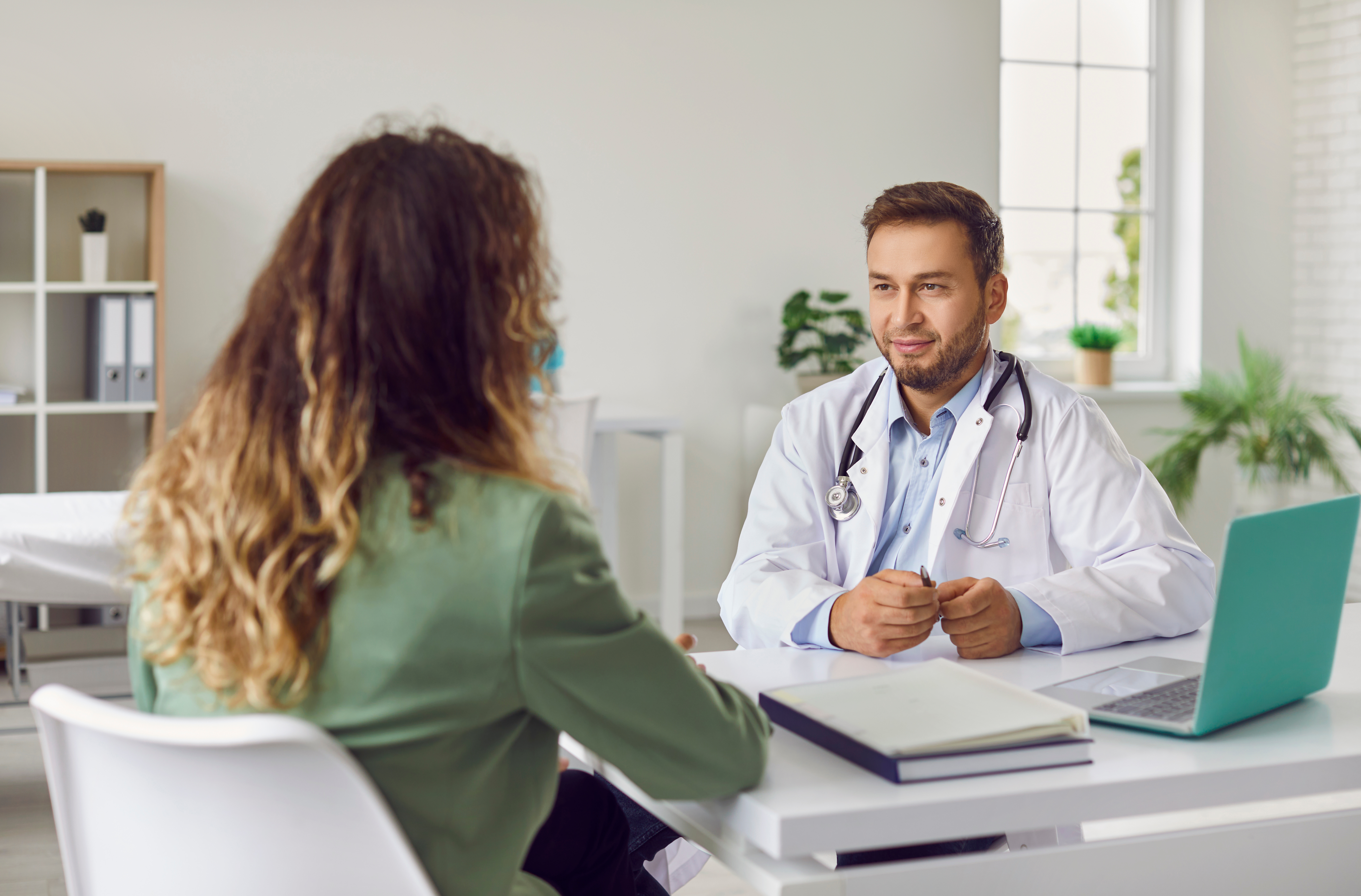 Arzt sitzt an einem Schreibtisch und spricht mit einer Patientin, die ihm gegenübersitzt.