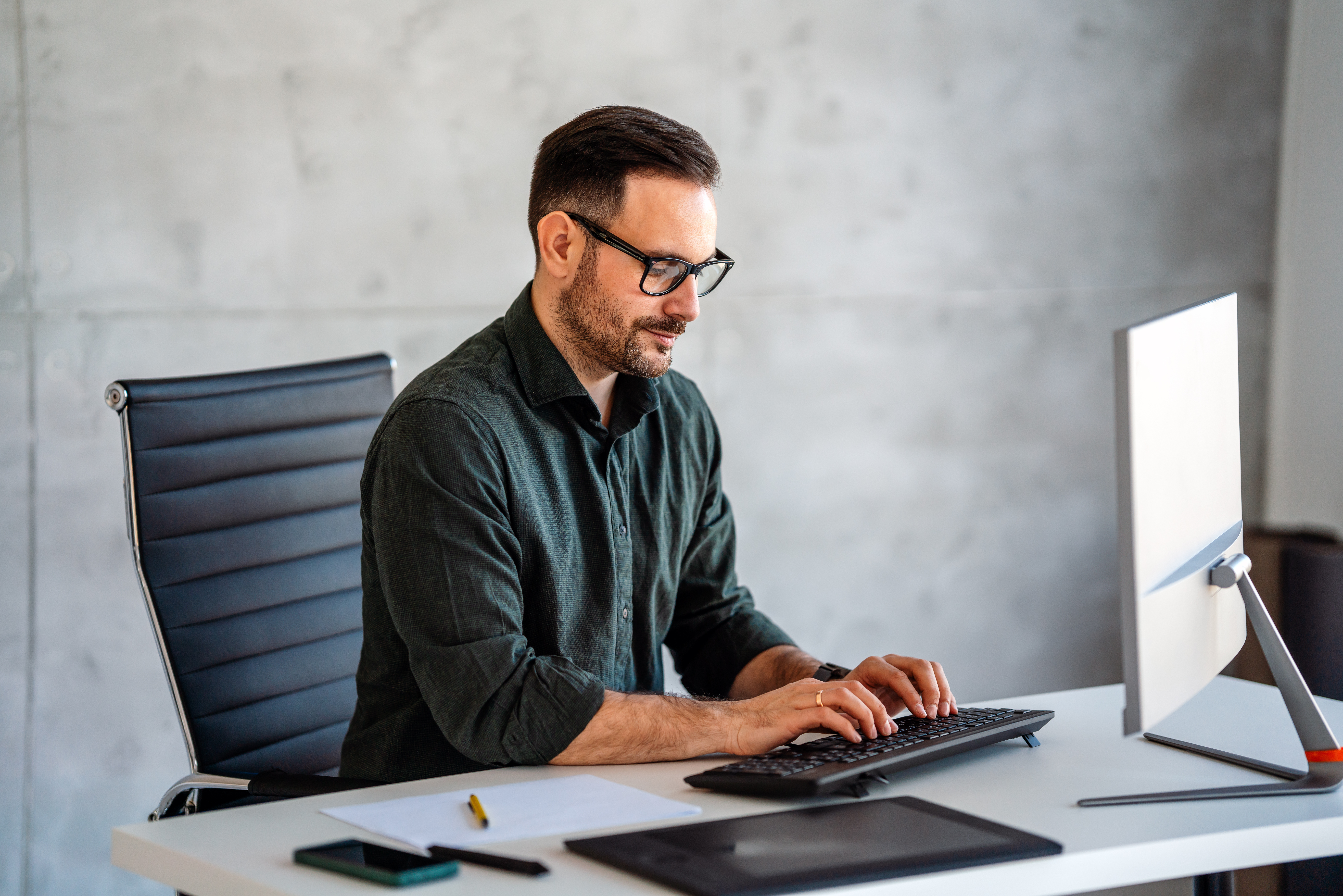 Mann mit Brille sitzt am Schreibtisch vor einem Laptop und arbeitet konzentriert.